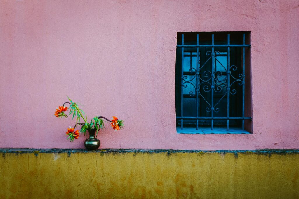 Pink and yellow wall with a flower vase and decorative window in Sevilla, Spain.